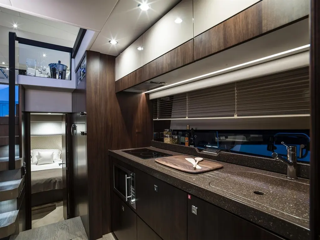Modern luxury kitchen with dark wood cabinetry, stone worktops, a sink, and a staircase leading to a bedroom area.